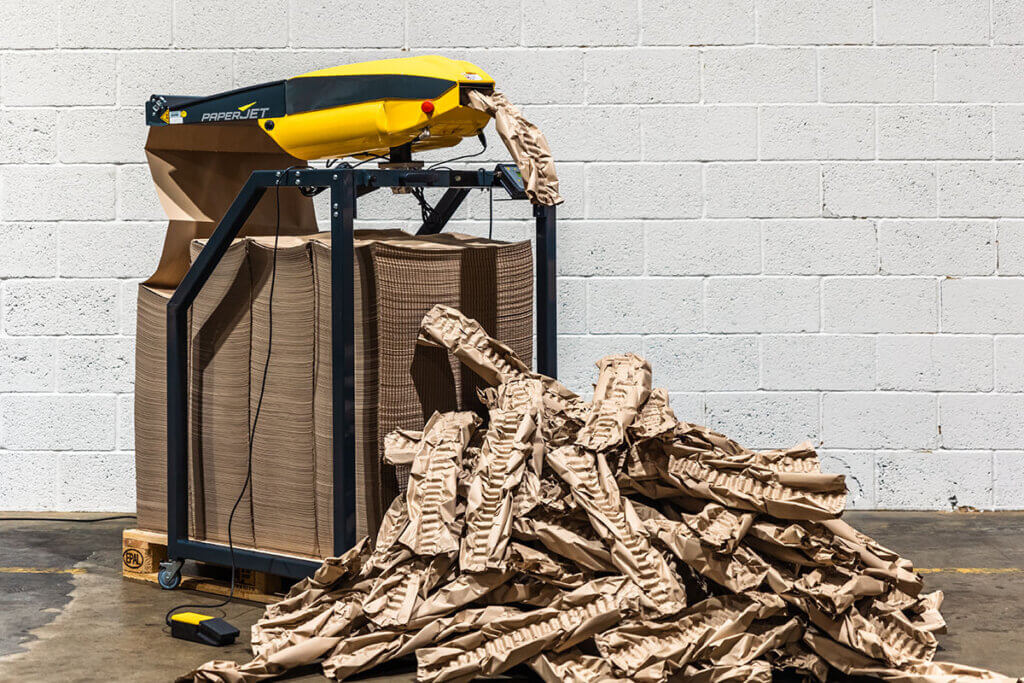 PaperJet machine with a pile of cushions on the floor against a white brick wall.